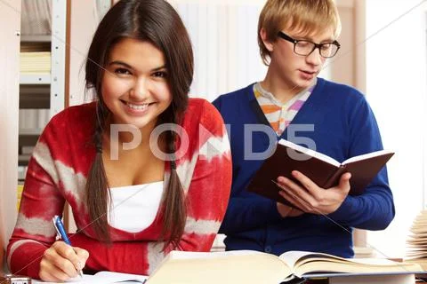 Portrait of young girl looking at camera on background of reading guy in college Stock Photos