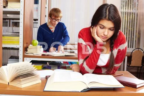 Portrait of young girl reading on background of guy in college library Stock Photos