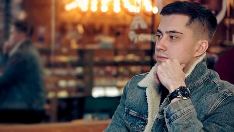 A portrait of a young guy looking around in a cozy coffee shop. Vídeos de archivo 108297582