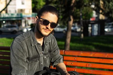 Portrait of young guy sitting on bench in the park. Stock Photos