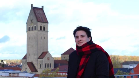 Portrait of young guy standing against backdrop of church.blue sky background Vidéo 262580319