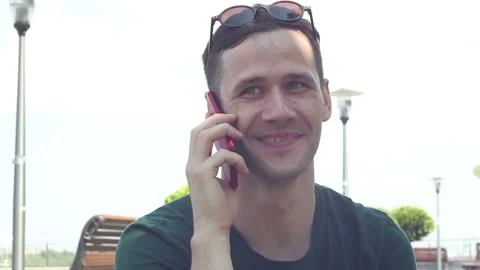 Portrait young guy  talking on the phone while sitting on the grass in the park. Video stock 111834960