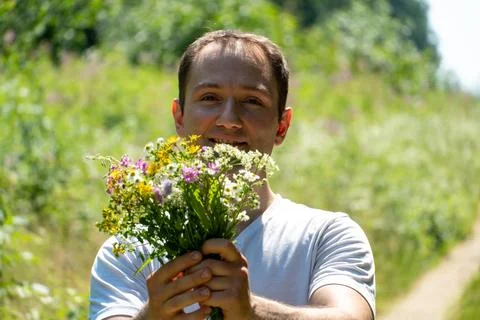 Portrait of a young guy in a white T-shirt and with a bouquet of flowers in h Stock Photos