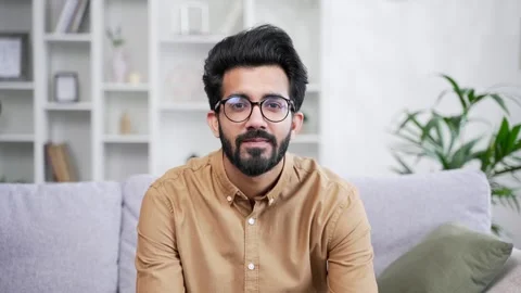Portrait of young handsome bearded man in shirt sitting on sofa in living room  Stock Footage 252206153
