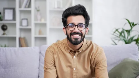 Portrait of young handsome bearded man in shirt sitting on sofa in living room  Stock Footage 252213311