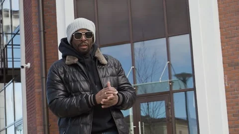 Portrait of young handsome black man, rubs hands stands on cityscape Stock Footage 238074816