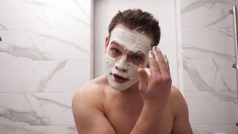 Portrait of young handsome man is applying fresh white thick mask and scrub on Stock Footage 123939490
