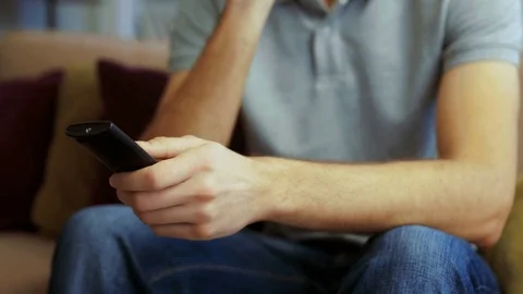 Portrait of young handsome man sitting on the couch and turning on TV with the Stock Footage 83145562