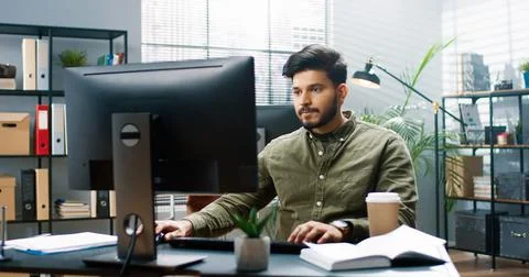 Portrait of young Hindu handsome bearded businessman texting on computer Stock Photos