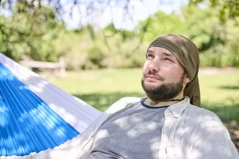 Portrait of a young hispanic man relaxed sitting in a hammock, resting outdoo Stock Photos