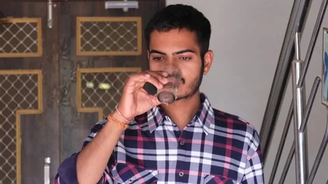 Portrait of a young Indian man drinking water from a glass indoors Видео 329922003