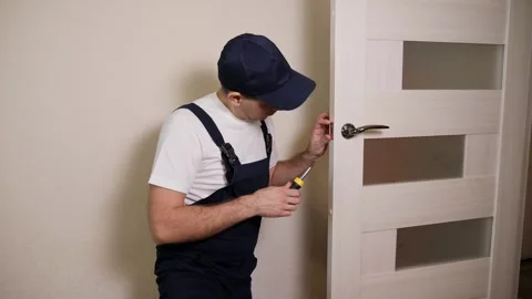 Portrait of young locksmith workman in blue uniform installing door knob. Stock Footage 287586036
