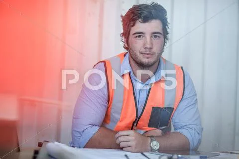 Portrait Of Young Male Construction Worker Sitting At Desk In Portable Cabin