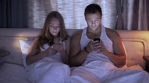 Portrait of a young man and his wife both using their smartphones while lying Vidéo 70921595