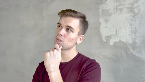 Portrait of young man on background of gray wall thought frowns eyebrows Video stock 120471544