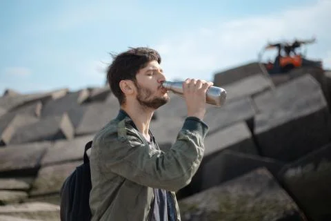 Portrait of young man with backpack, using reusable steel thermo water bottle. Stock Photos