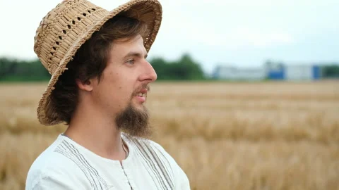 Portrait of a young man with a beard and straw hat standing in a wheat field Stock Footage 135590748