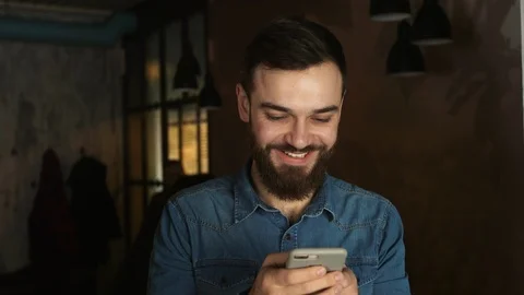 Portrait of a young man with a beard in a cafe. Blue shirt Man writes a message Vídeos de archivo 100597719