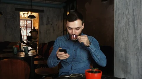 Portrait of a young man with a beard in a cafe. Blue shirt Man writes a message Vídeos de archivo 100603284