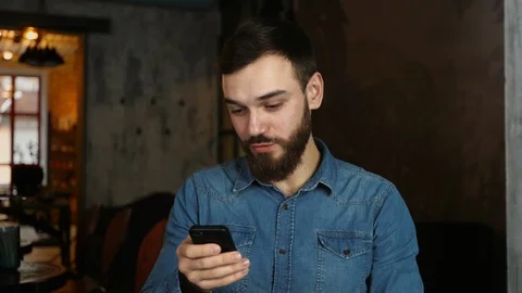 Portrait of a young man with a beard in a cafe. Blue shirt Man writes a message Stock Footage 100603412