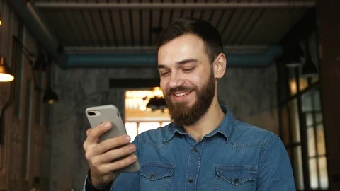 Portrait of a young man with a beard in a cafe. Blue shirt Man uses video call Stock Footage 100604958