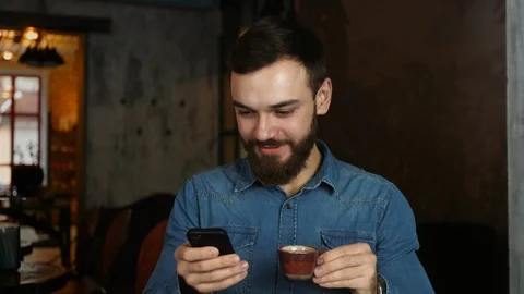 Portrait of a young man with a beard in a cafe. Blue shirt Man writes a message Video stock 100772155