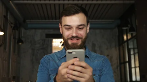 Portrait of a young man with a beard in a cafe. Blue shirt Man writes a message Stock Footage 100773675