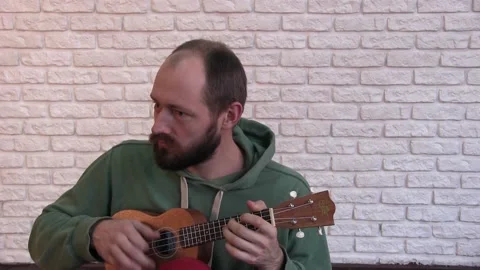 Portrait of a young man with a beard playing the ukulele 動画素材 131381849
