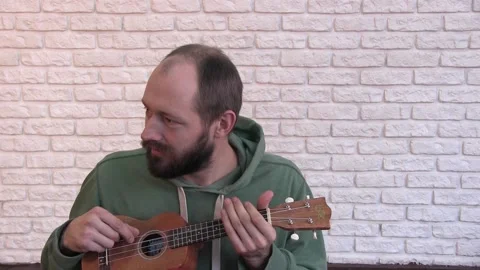Portrait of a young man with a beard playing the ukulele Vidéo 131381941