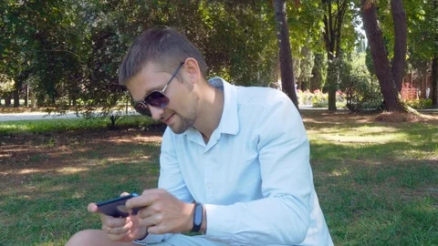 Portrait of a young man with a beard sitting in the Park and using the phone for Stock Footage 113948581