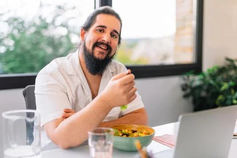Portrait of young man with beard while eating salad, smiling Stock Photos