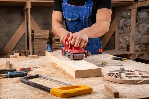Portrait of a  young man  carpenter using electric sanding machine to polish  Stock Photos