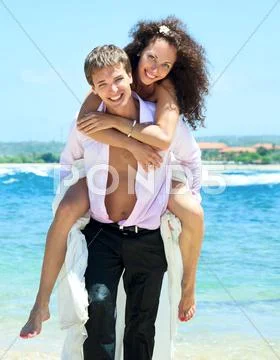 Portrait Of Young Man Carrying His Cute Young Girlfriend On His Back. The Hap