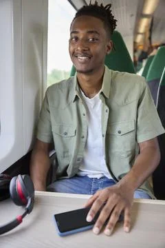 Portrait Of Young Man Commuting To Work Sitting  On Train With Wireless Hea.. Stock Photos