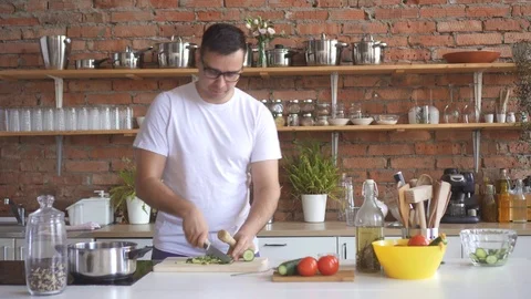 Portrait of a young man dancing and singing in the kitchen, he cuts vegetables Video stock 98311192