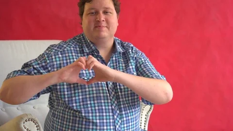 Portrait of a young man doing a heart gesture against a red background Stock Footage 82381066