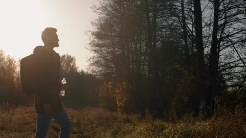 Portrait young man drinking water from bottle in sunset light standing in meadow Stock Footage 119009003