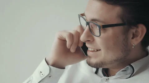 Portrait of Young Man In Glasses Talking on The Phone Against White Background Stock Footage 62543207