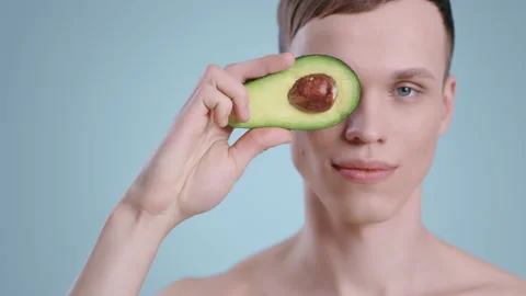 Portrait of young man holding half of avocado in front of face and smiling while Stock Footage