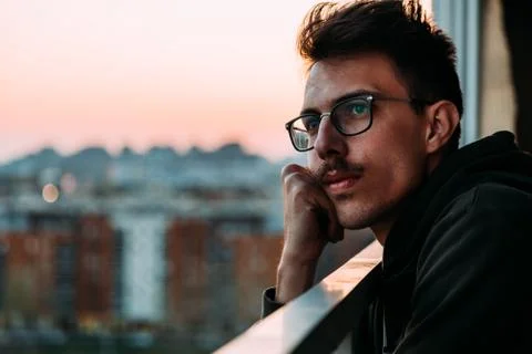 Portrait of a young man looking at sunset from a balcony thinking about life Stock Photos