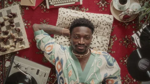 Portrait of Young Man Lying on Vintage Rug among Retro Vinyl and Chessboard Stock Footage 339852970