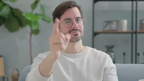 Portrait of Young Man Pointing at Camera Sitting on Sofa at Home Stock Footage 286163655