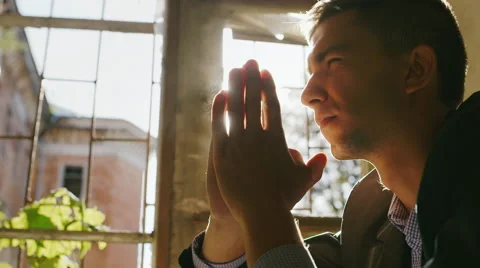 Portrait of a young man praying in the sun. Sitting by the window in an old Видео 67353169