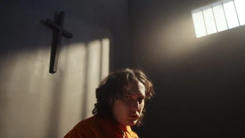 Portrait of Young Man in Prison Cell Sitting under Wall Cross Stock Footage 310336904
