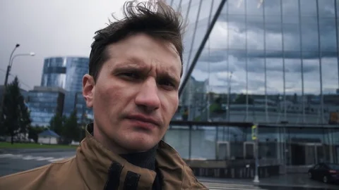 Portrait of young man in rain jacket. Business centre building at background Stock Footage 79415684