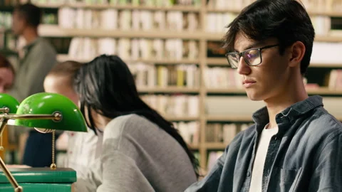 Portrait of young man reading open book at library study table Stock Footage 336360784