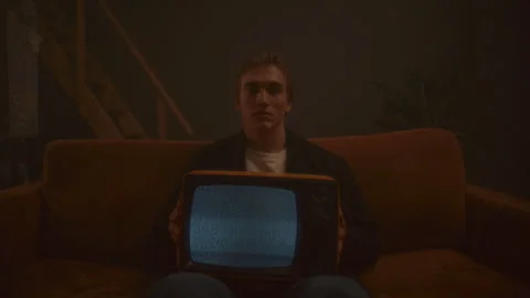 Portrait of Young Man Sitting on Sofa, Holding Vintage TV with Static Screen Stock Footage 307549994