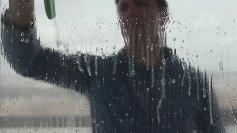 Portrait of young man sprays window cleaner on big window and washes it Vídeo Stock 137769855