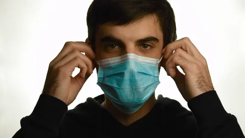 Portrait of a young man taking off his medical mask and smiling on a white Vídeos de archivo 128456828