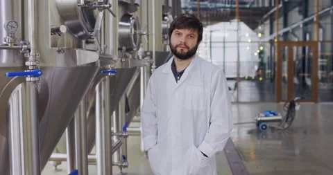 Portrait of young man technologist in lab coat posing at camera in brewery plant Stock Footage 148395941